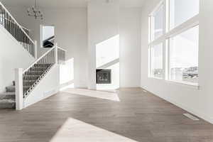 Unfurnished living room with an inviting chandelier, a towering ceiling, and hardwood / wood-style flooring