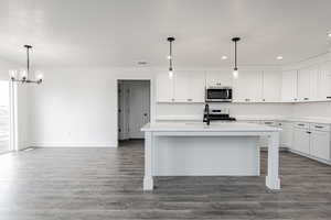 Kitchen featuring white cabinetry, hanging light fixtures, an inviting chandelier, an island with sink, and appliances with stainless steel finishes