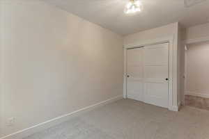 Unfurnished bedroom featuring a textured ceiling, a closet, and light colored carpet