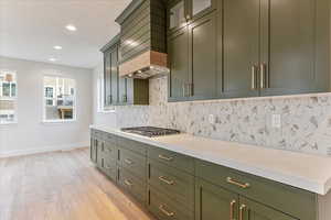 Kitchen featuring light hardwood / wood-style floors, custom exhaust hood, decorative backsplash, and stainless steel gas stovetop