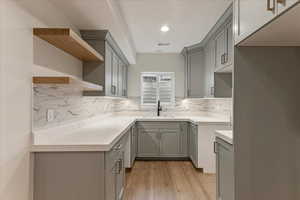 Kitchen with gray cabinets, light hardwood / wood-style floors, tasteful backsplash, and sink