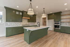 Kitchen with appliances with stainless steel finishes, custom range hood, tasteful backsplash, and green cabinetry