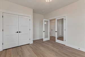 Unfurnished bedroom featuring a closet, french doors, and light wood-type flooring