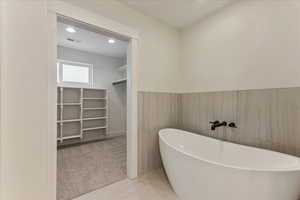 Bathroom featuring tile patterned flooring, tile walls, and a tub to relax in