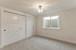 Unfurnished bedroom with a closet, a textured ceiling, and light colored carpet