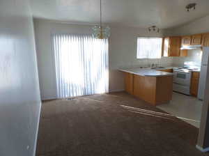 Kitchen featuring a chandelier, white appliances, light carpet, lofted ceiling, and kitchen peninsula