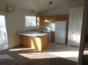 Kitchen with plenty of natural light, kitchen peninsula, white appliances, and vaulted ceiling