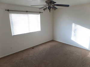 Carpeted empty room with a healthy amount of sunlight and ceiling fan