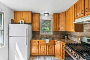 Kitchen with white fridge, gas stove, sink, light tile floors, and backsplash