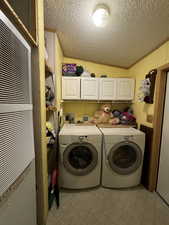 Laundry area with light tile patterned flooring, washer and clothes dryer, a textured ceiling, and cabinets