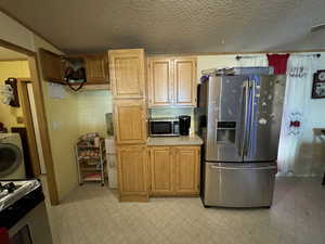 Kitchen with washer / clothes dryer, appliances with stainless steel finishes, a textured ceiling, and light tile patterned floors