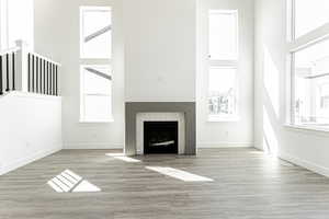 Unfurnished living room with a tiled fireplace, baseboards, wood finished floors, and a towering ceiling