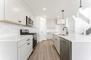 Kitchen featuring tasteful backsplash, hanging light fixtures, a sink, appliances with stainless steel finishes, and light wood-style flooring
