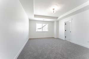 Spare room featuring a textured ceiling, visible vents, light carpet, a raised ceiling, and baseboards