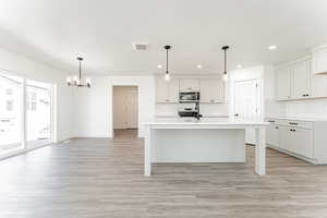 Kitchen featuring light wood-style flooring, tasteful backsplash, light countertops, stainless steel appliances, and a notable chandelier
