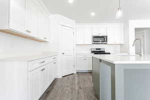 Kitchen featuring white cabinetry, stainless steel appliances, light countertops, recessed lighting, and wood finished floors