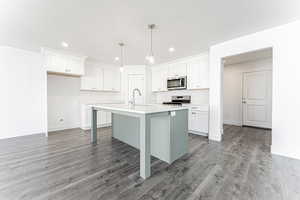Kitchen with white cabinetry, a sink, appliances with stainless steel finishes, light wood-type flooring, and a center island with sink