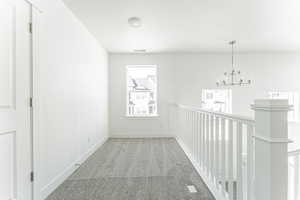 Hallway with a notable chandelier, visible vents, carpet floors, and baseboards