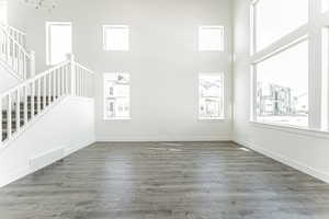 Unfurnished living room featuring visible vents, a healthy amount of sunlight, a high ceiling, and stairway