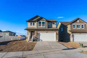 View of front of home featuring stone siding, an attached garage, concrete driveway, and fence