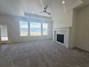 Unfurnished living room featuring a tray ceiling, a brick fireplace, carpet floors, and ceiling fan