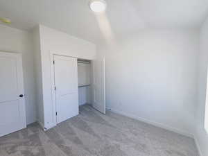 Unfurnished bedroom featuring a closet, carpet floors, and lofted ceiling