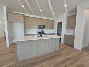 Kitchen featuring tasteful backsplash, appliances with stainless steel finishes, light wood-type flooring, and an island with sink