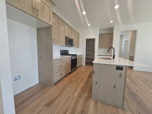 Kitchen with an island with sink, sink, appliances with stainless steel finishes, light hardwood / wood-style flooring, and backsplash