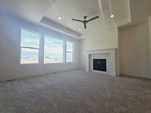 Unfurnished living room with carpet floors, a brick fireplace, ceiling fan, and a raised ceiling