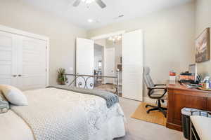 Carpeted bedroom featuring ceiling fan with notable chandelier and a closet