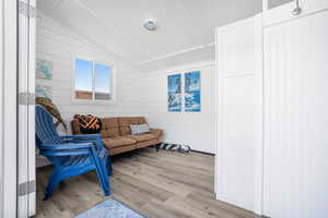 Living room featuring vaulted ceiling, wooden walls, and light hardwood / wood-style floors