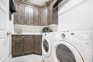 Washroom with light tile patterned floors, independent washer and dryer, and cabinets