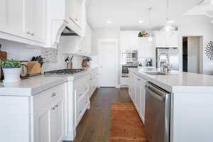 Kitchen featuring tasteful backsplash, sink, dark wood-type flooring, appliances with stainless steel finishes, and a kitchen island with sink