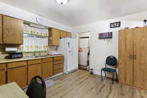 Kitchen featuring stacked washer / dryer, white fridge with ice dispenser, light hardwood / wood-style flooring, backsplash, and sink