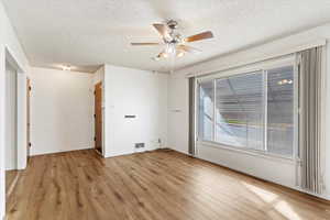 Empty room with a textured ceiling, light wood-type flooring, and ceiling fan