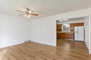 Unfurnished living room featuring ceiling fan, sink, light hardwood / wood-style floors, and a textured ceiling