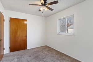 Carpeted empty room with ceiling fan and a textured ceiling