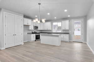 Kitchen featuring decorative light fixtures, a wealth of natural light, a kitchen island, and appliances with stainless steel finishes