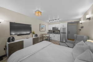 Bedroom with stainless steel refrigerator, track lighting, and hardwood / wood-style floors