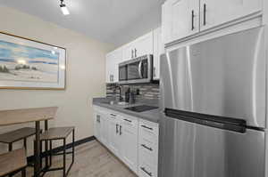 Kitchen with light hardwood / wood-style flooring, white cabinets, backsplash, and stainless steel appliances