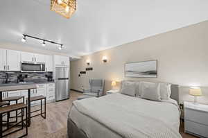 Bedroom with light hardwood / wood-style floors, sink, stainless steel refrigerator, and rail lighting