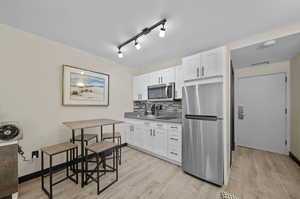 Kitchen with rail lighting, light wood-type flooring, white cabinets, backsplash, and stainless steel appliances