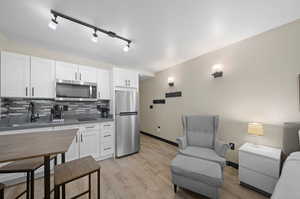 Kitchen with white cabinetry, stainless steel appliances, light wood-type flooring, backsplash, and track lighting