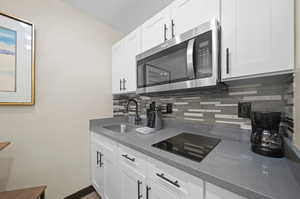 Kitchen with black electric cooktop, white cabinets, backsplash, stone countertops, and sink