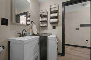 Washroom with washing machine and clothes dryer, sink, and light wood-type flooring