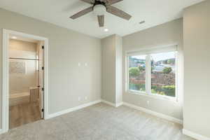 Unfurnished bedroom with ensuite bathroom, ceiling fan, and light colored carpet