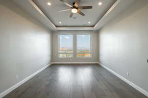 Empty room with ceiling fan, dark hardwood / wood-style floors, and a tray ceiling