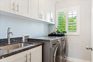 Washroom with cabinets, washing machine and clothes dryer, and sink