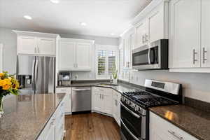 Kitchen featuring dark hardwood / wood-style flooring, dark stone countertops, white cabinets, and stainless steel appliances