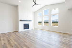 Unfurnished living room with light hardwood / wood-style flooring, vaulted ceiling, and ceiling fan